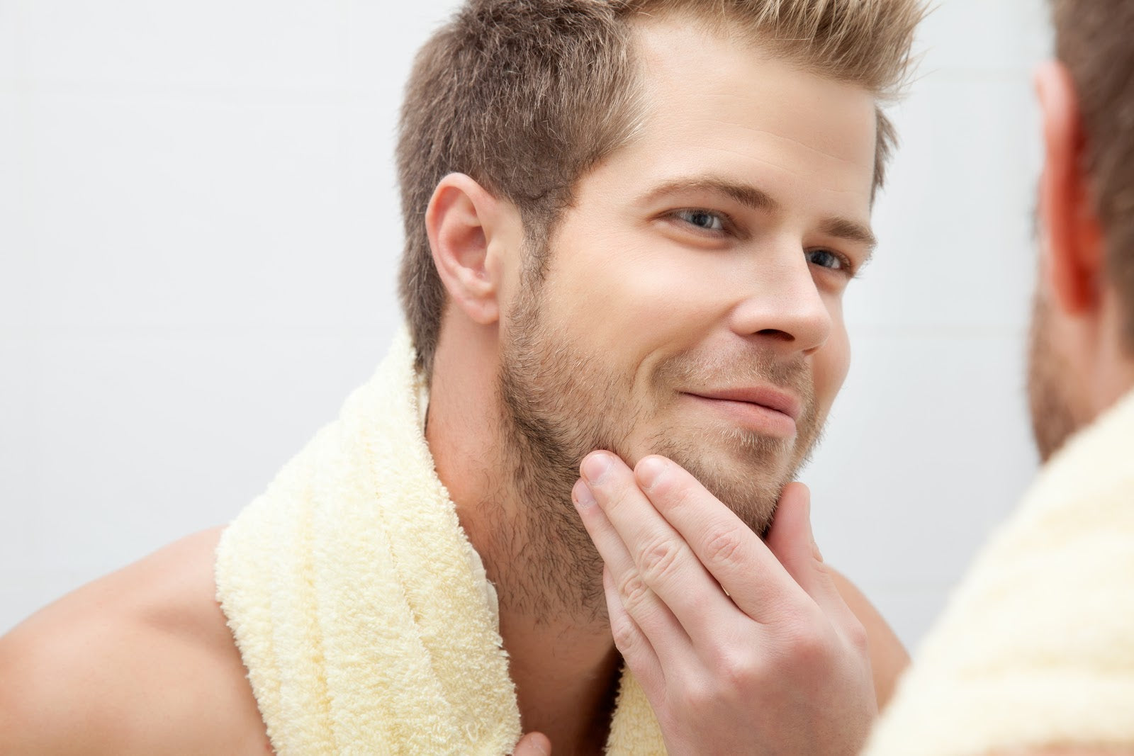 A man leaning toward a bathroom mirror, closely examining his cheeks and jawline