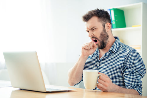 man yawning in front of laptop