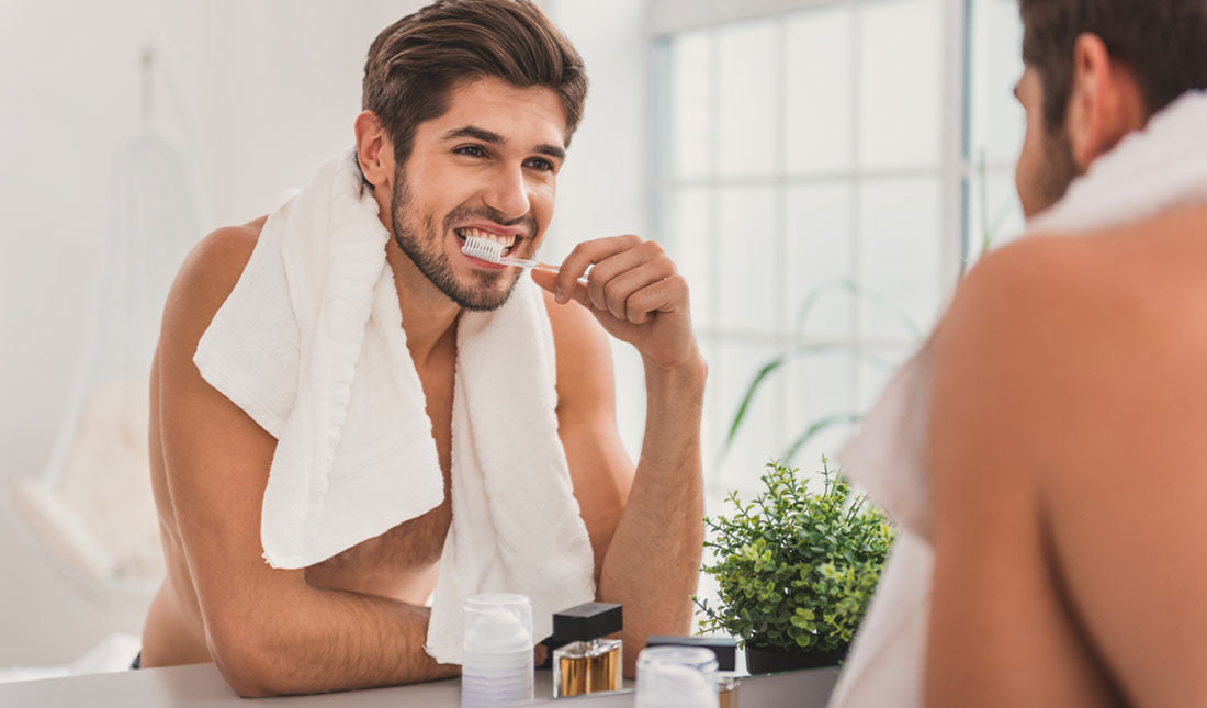 man brushing teeth by mirror