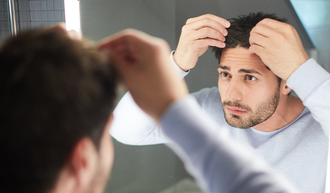 man looking at his forehead and scalp in the mirror