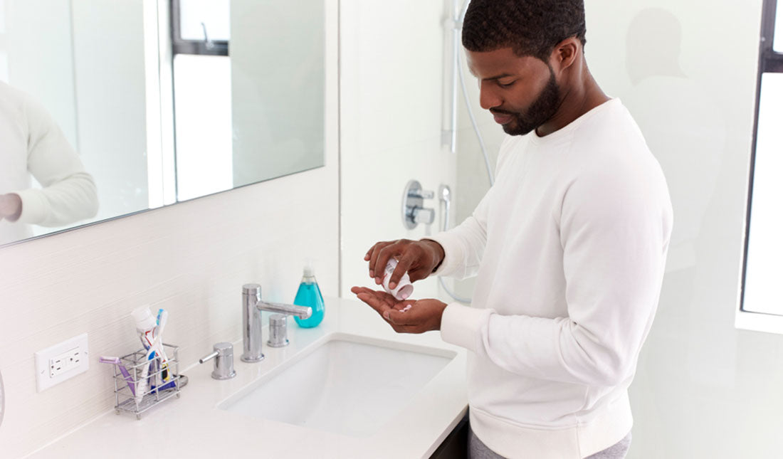 A man taking a daily supplement with a glass of water